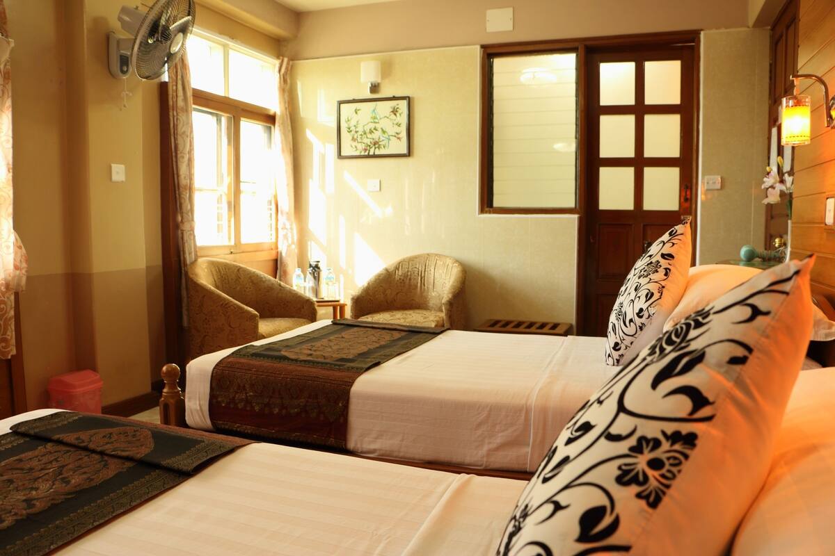A hotel room with two beds, a chair, a window, and a wall-mounted fan.