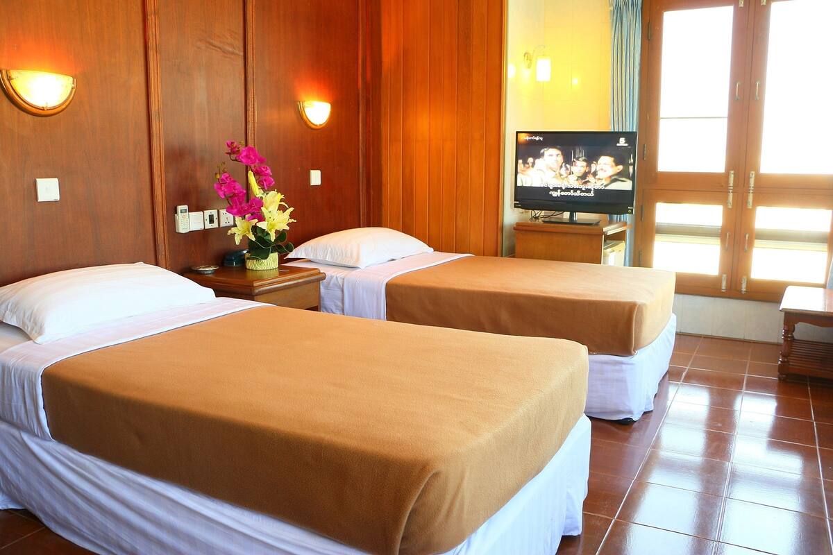 A hotel room with two beds, wooden paneling, a television, and a window with curtains.