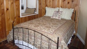 Un dormitorio con cama, un rincón de lectura junto a la ventana y paneles de madera.