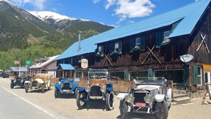 Una hilera de coches antiguos estacionados frente a un edificio rústico con un cartel que dice 'Twin Lakes Inn'.