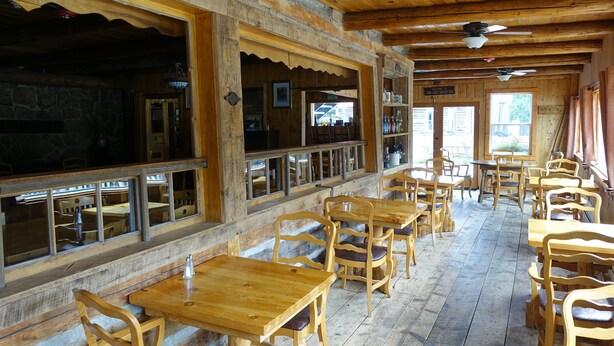 Un interior rústico de madera con varias mesas y sillas de madera, ventanas amplias y una pared de piedra.