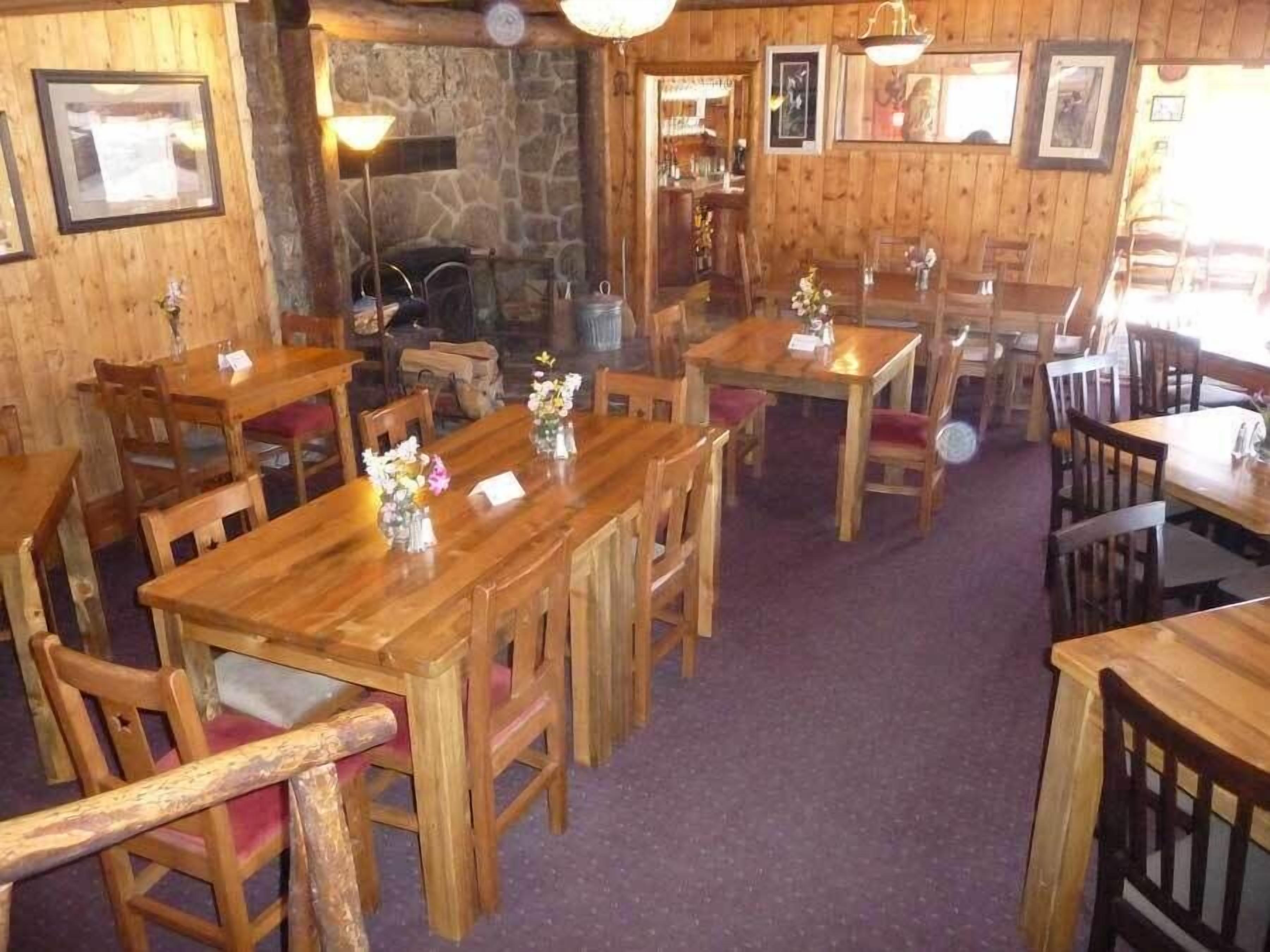 Um interior rústico de madeira com várias mesas e cadeiras de madeira, paredes de pedra e quadros nas paredes.