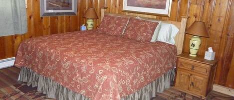 Una habitación con paneles de madera, una cama grande, dos mesitas de noche con lámparas y dos cuadros en las paredes.