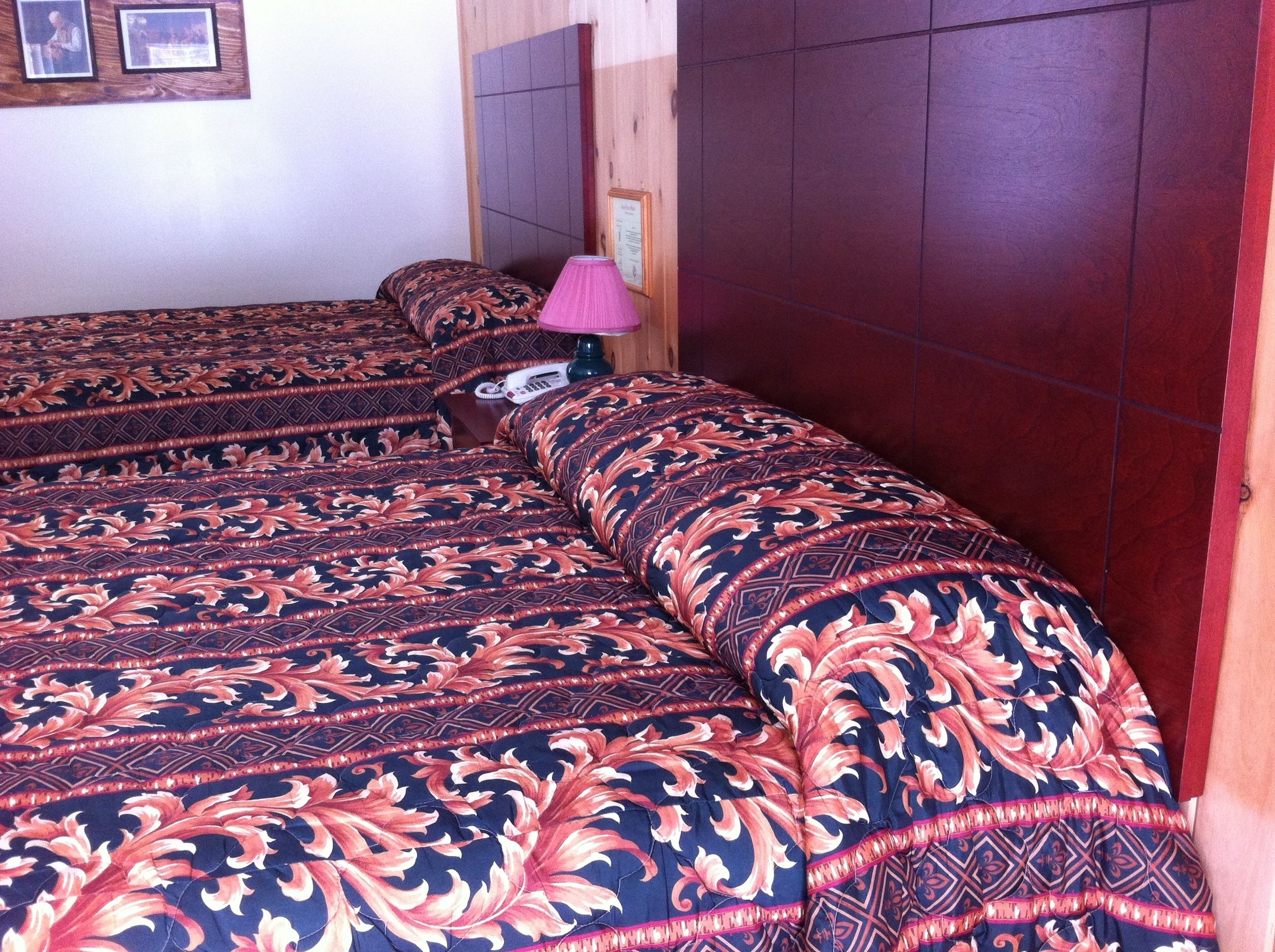A bed with a patterned bedspread, a wooden headboard, and a bedside lamp.