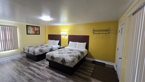 A hotel room with two beds, a painting on the wall, a bedside lamp, and a coat rack.