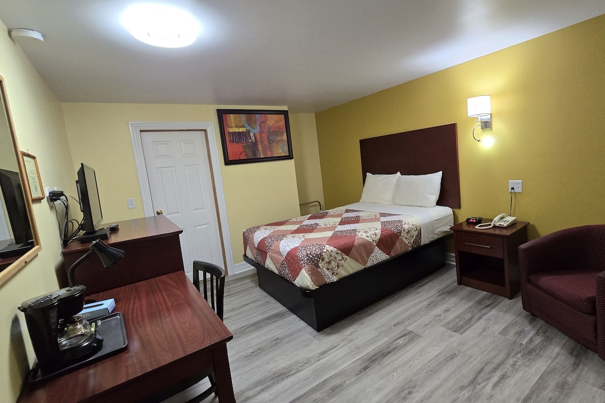 A hotel room with a bed, desk, chair, and a nightstand with a phone.