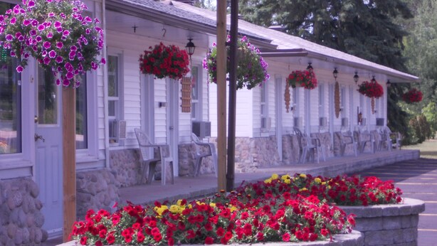 A row of white buildings with hanging flower baskets and a stone planter with red and yellow flowers in front.
