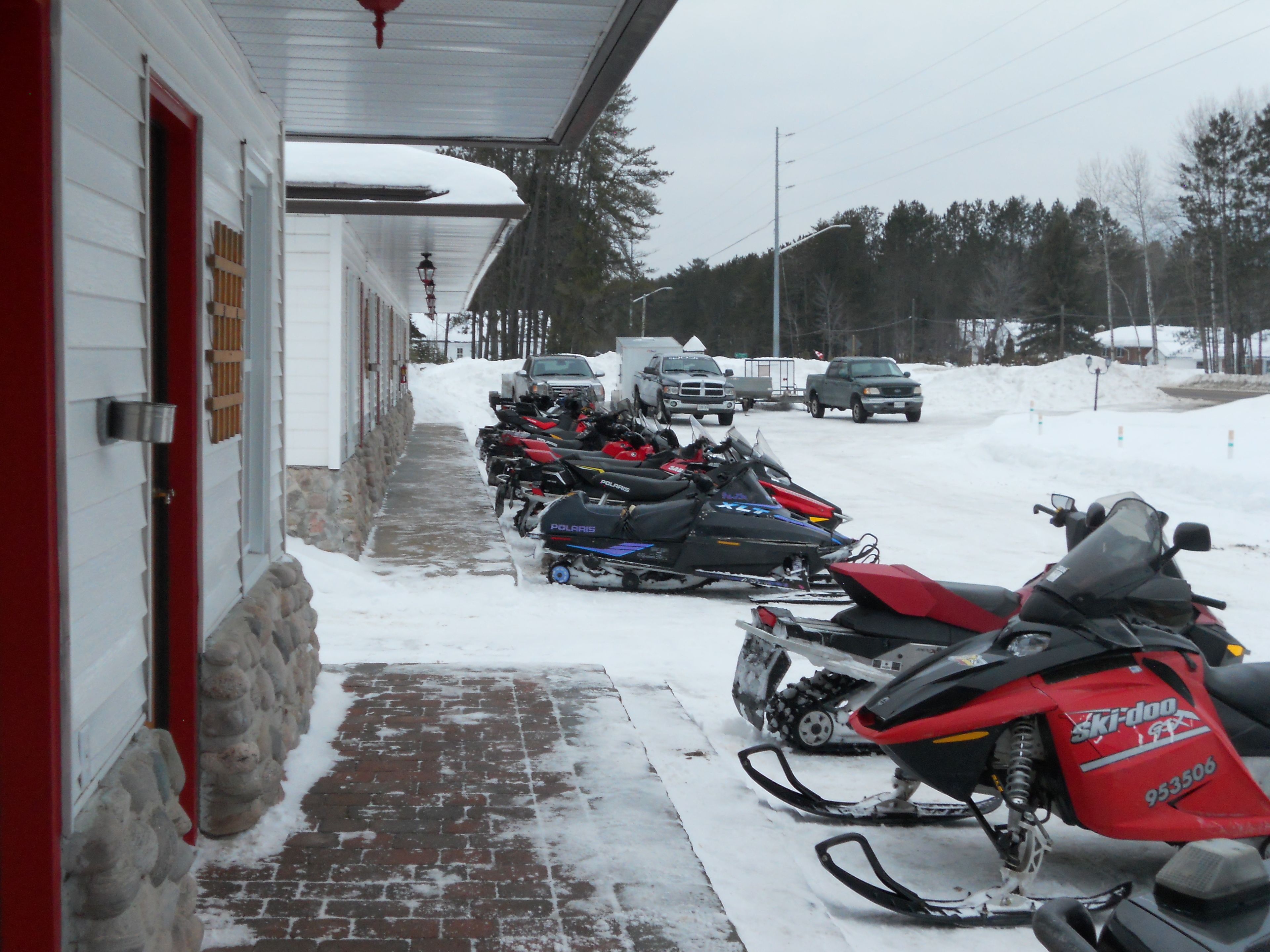 A row of snowmobiles parked outside a building with a brick pathway leading to the entrance.