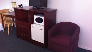A compact room with a wooden desk, a television on a stand, a small refrigerator, and a single chair.
