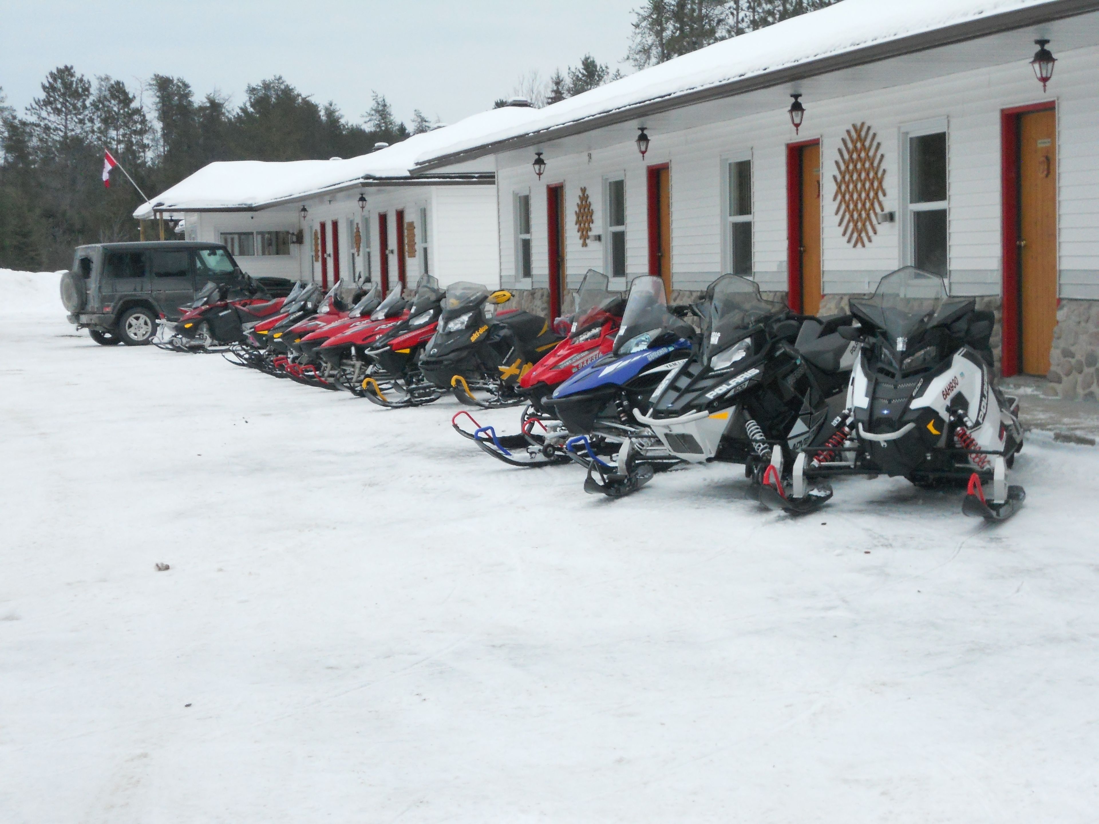 A row of snowmobiles parked in front of a building with a row of doors and windows.