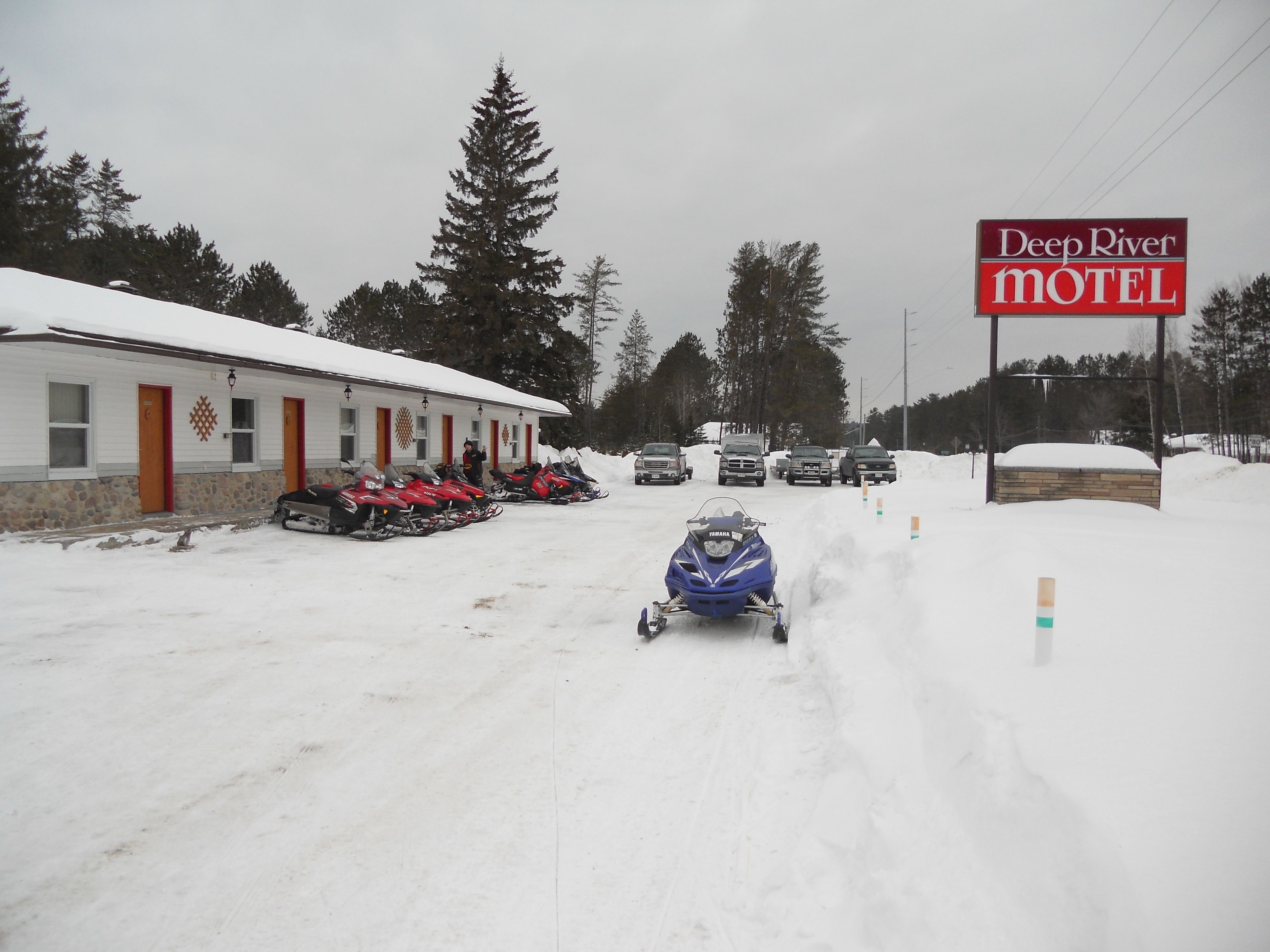 A snow-covered road with a snowmobile in motion, a motel sign, and several parked snowmobiles.