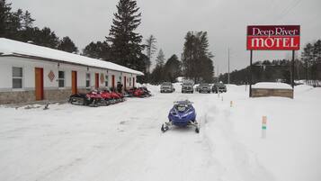 A snow-covered road with a snowmobile in motion, a motel sign, and several parked snowmobiles.
