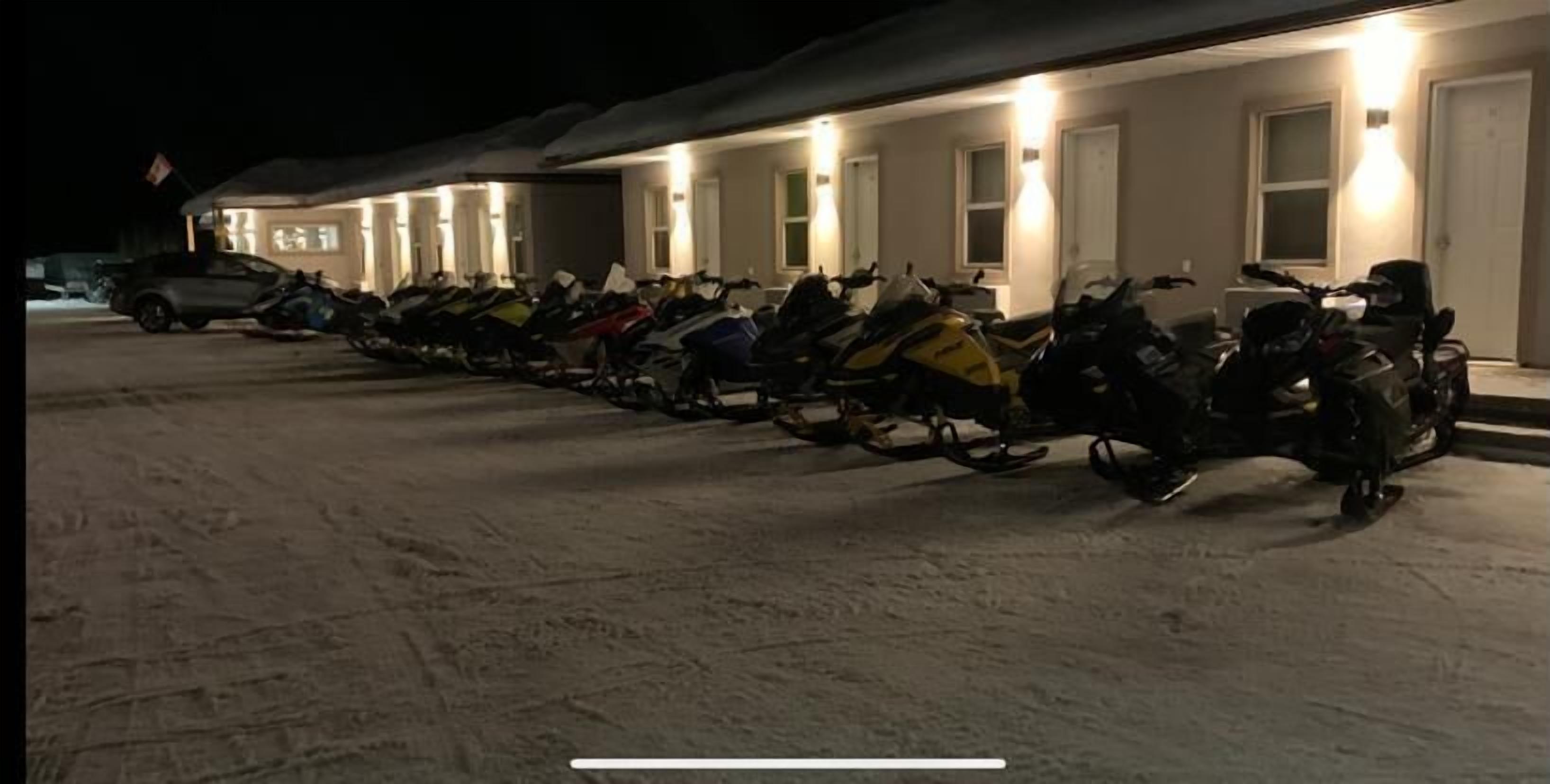 A row of snowmobiles parked in front of a building with multiple doors and windows, suggesting a facility or lodge.