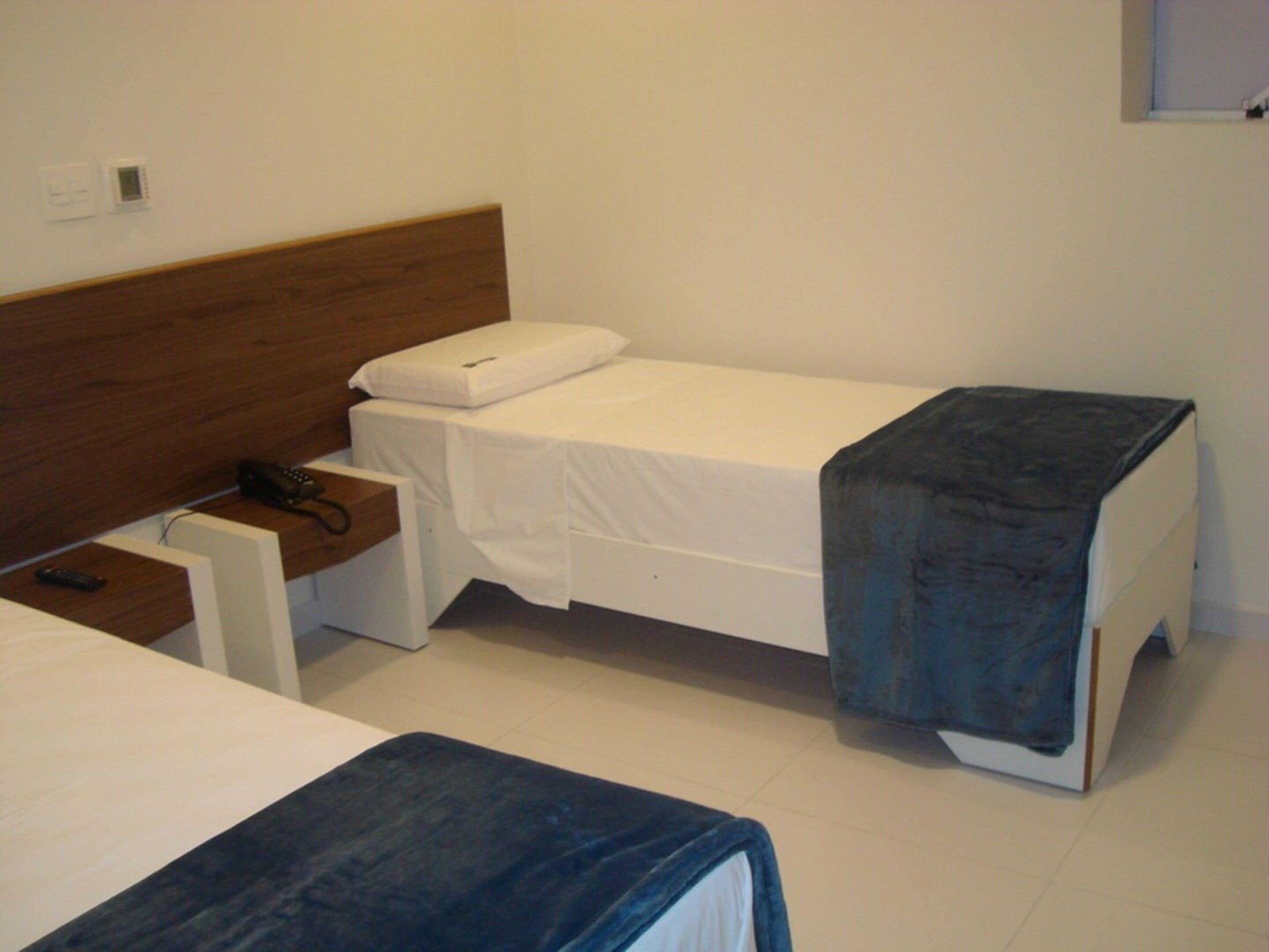 A small, clean room with two single beds, a wooden headboard, a bedside table with a phone, and a small desk with a chair.