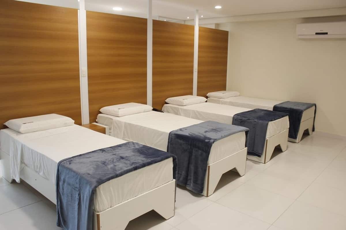 A room with four beds arranged in a row, each with a white mattress and a blue blanket.