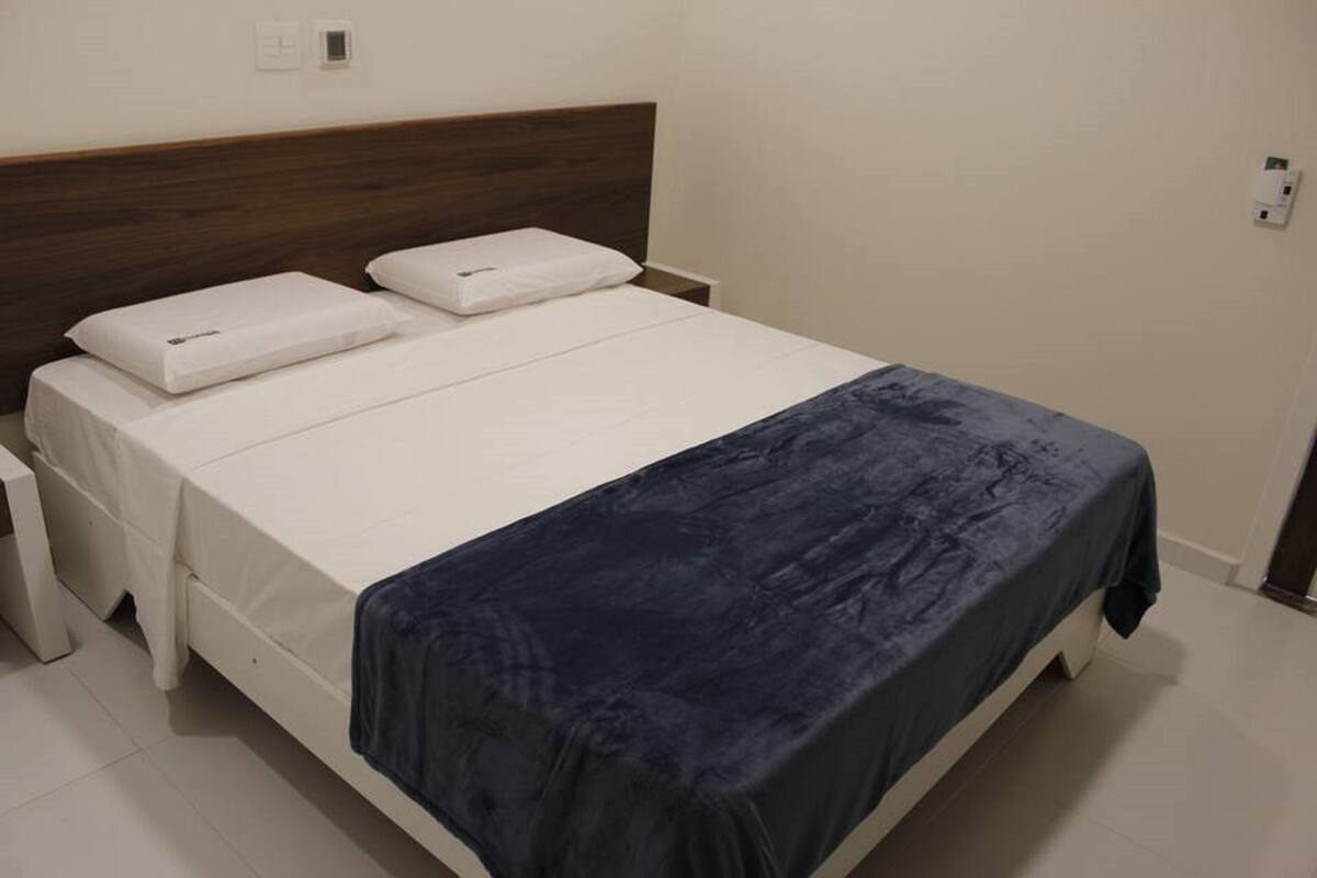 A double bed with a wooden headboard, white bedding, and a dark blue blanket.