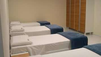 A hotel room with four single beds, each with a white mattress and blue headboard. There is a wooden wardrobe against the wall and an air conditioning unit mounted on the ceiling.