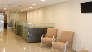 A reception area with a glass partition, beige chairs, and a flat-screen TV on the wall.