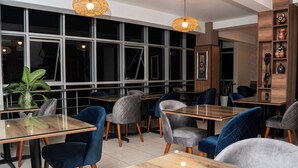 Un comedor moderno con mesas de vidrio y sillas acolchadas, ventanas amplias y estanterías decorativas.