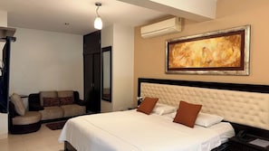 Quarto de hotel com uma cama grande, um sofá, um quadro na parede e um aparelho de ar condicionado.