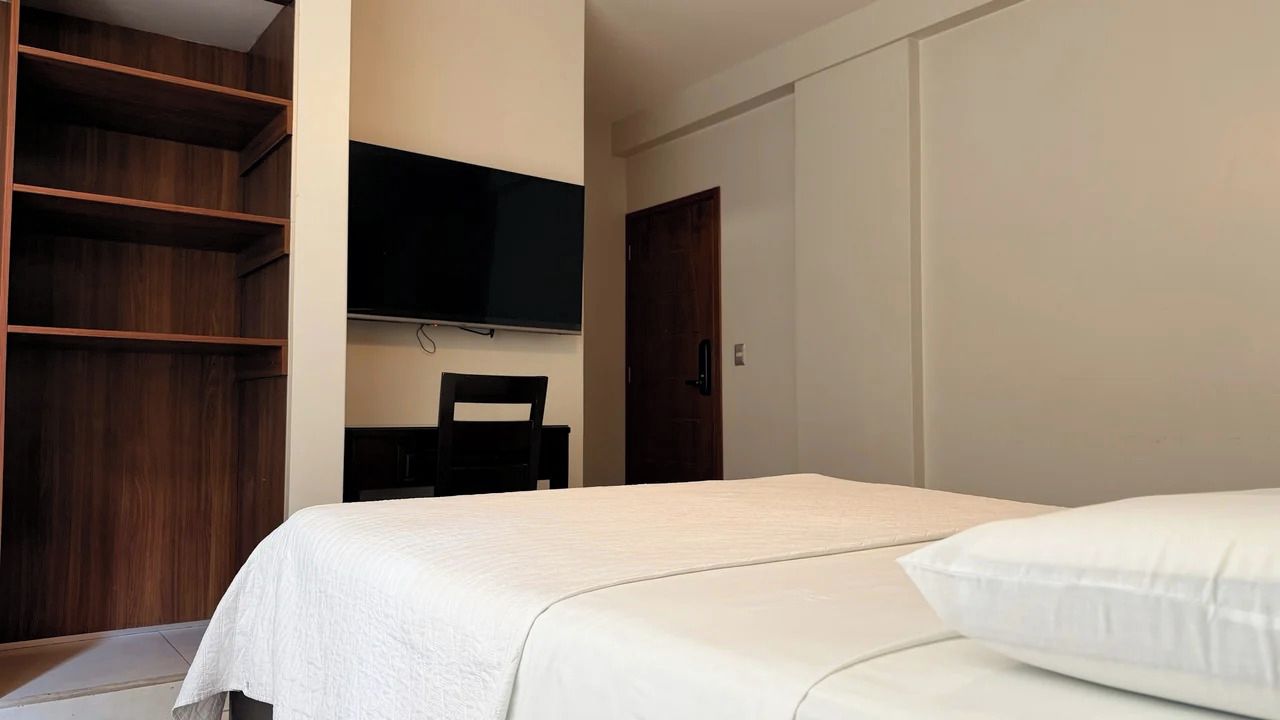 Un dormitorio con cama, televisión montada en la pared y armario.