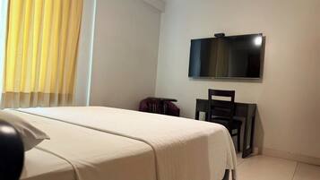 Habitació d'hotel amb un llit, un televisor penjat a la paret, una cadira i un escriptori.