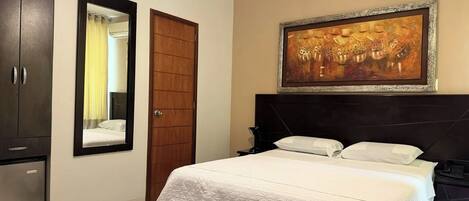 Una habitación de hotel con una cama, un armario, un espejo y un cuadro en la pared.
