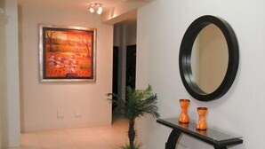 A hallway with a framed painting, a round mirror, and two orange vases on a black console table. - El Cacique Hotel (Piura)