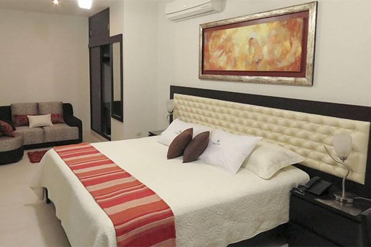 A hotel room with a large bed, a sofa, a bedside table, and a painting on the wall.