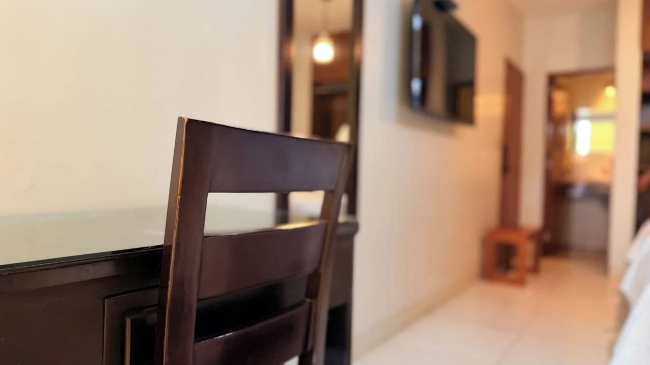 Une chaise en bois à la teinte foncée, placée devant une table à manger dans une pièce dont le mur est blanc et où est suspendu un luminaire.