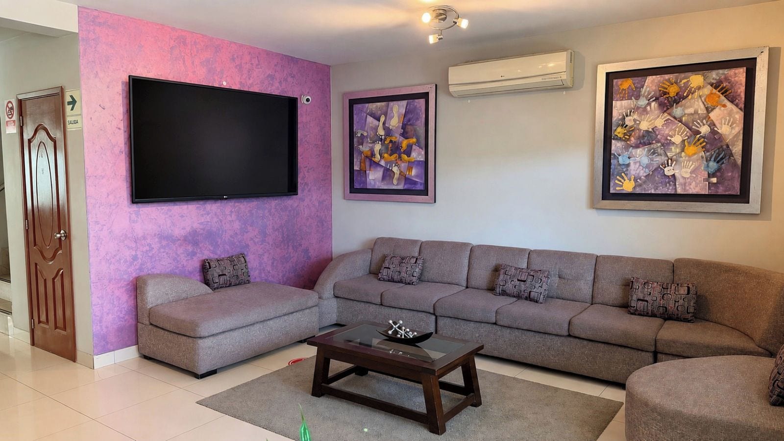 A living room with a sofa set, a coffee table, and two wall-mounted flat-screen TVs.