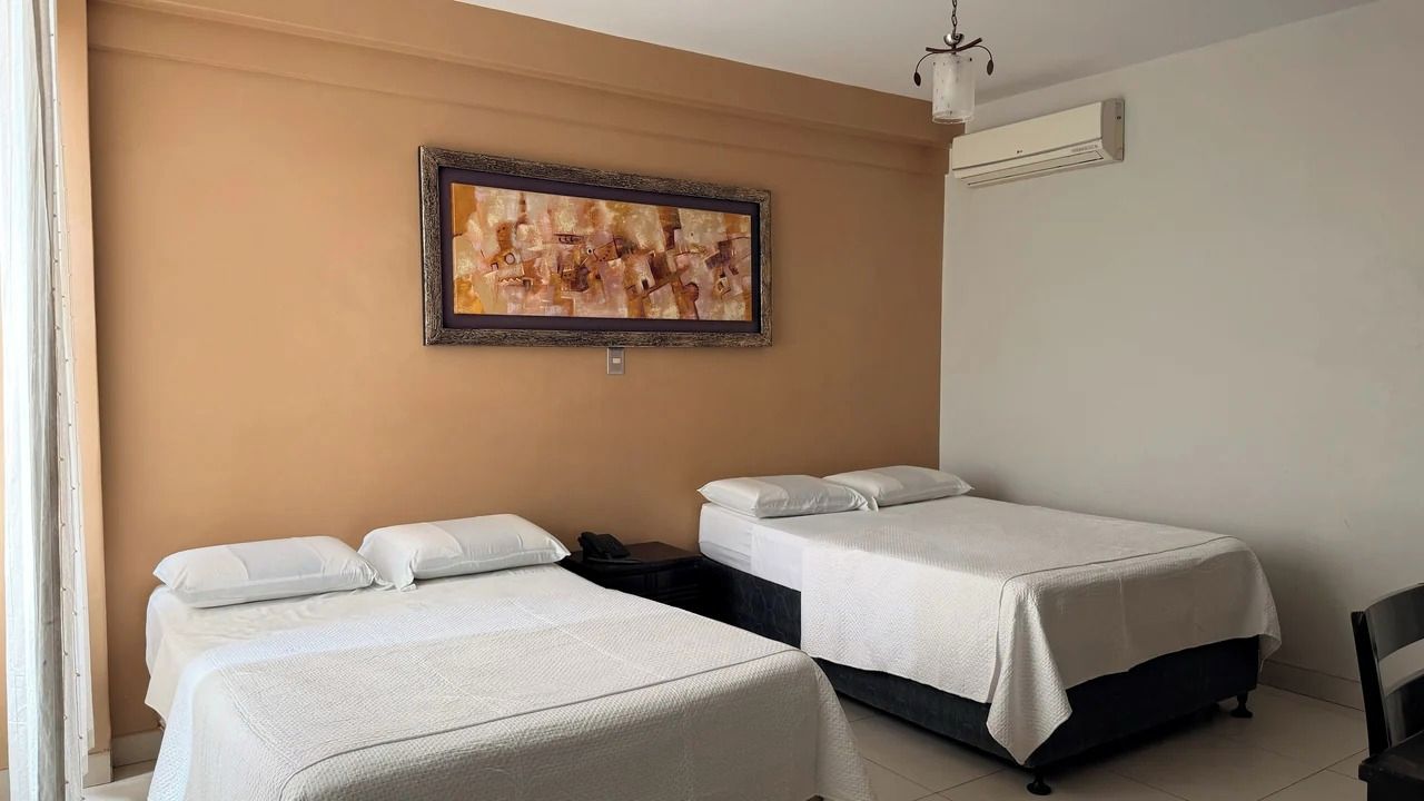 Habitación de hotel con dos camas, un cuadro abstracto enmarcado en la pared y un equipo de aire acondicionado.