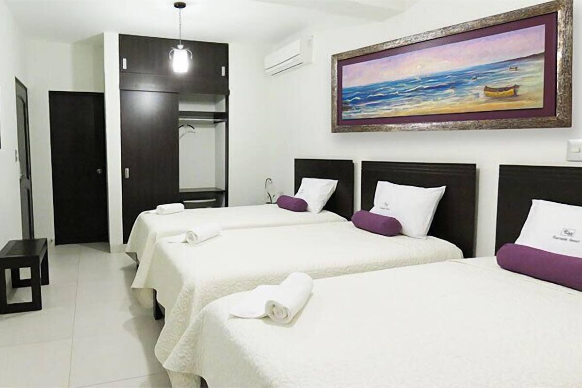 A hotel room with two beds, a wardrobe, a television, and a painting of a beach scene.