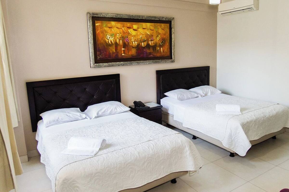 A hotel room with two beds, a painting on the wall, and a chair.