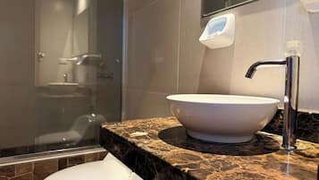 Un baño con un lavabo blanco, cabina de ducha con mampara de vidrio y encimera de mármol.