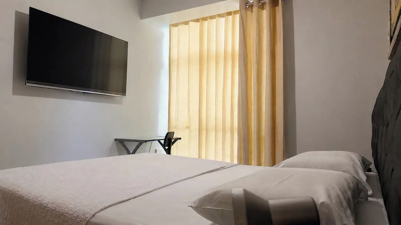 Habitació d'hotel amb un llit, un televisor penjat a la paret i una finestra amb cortines.