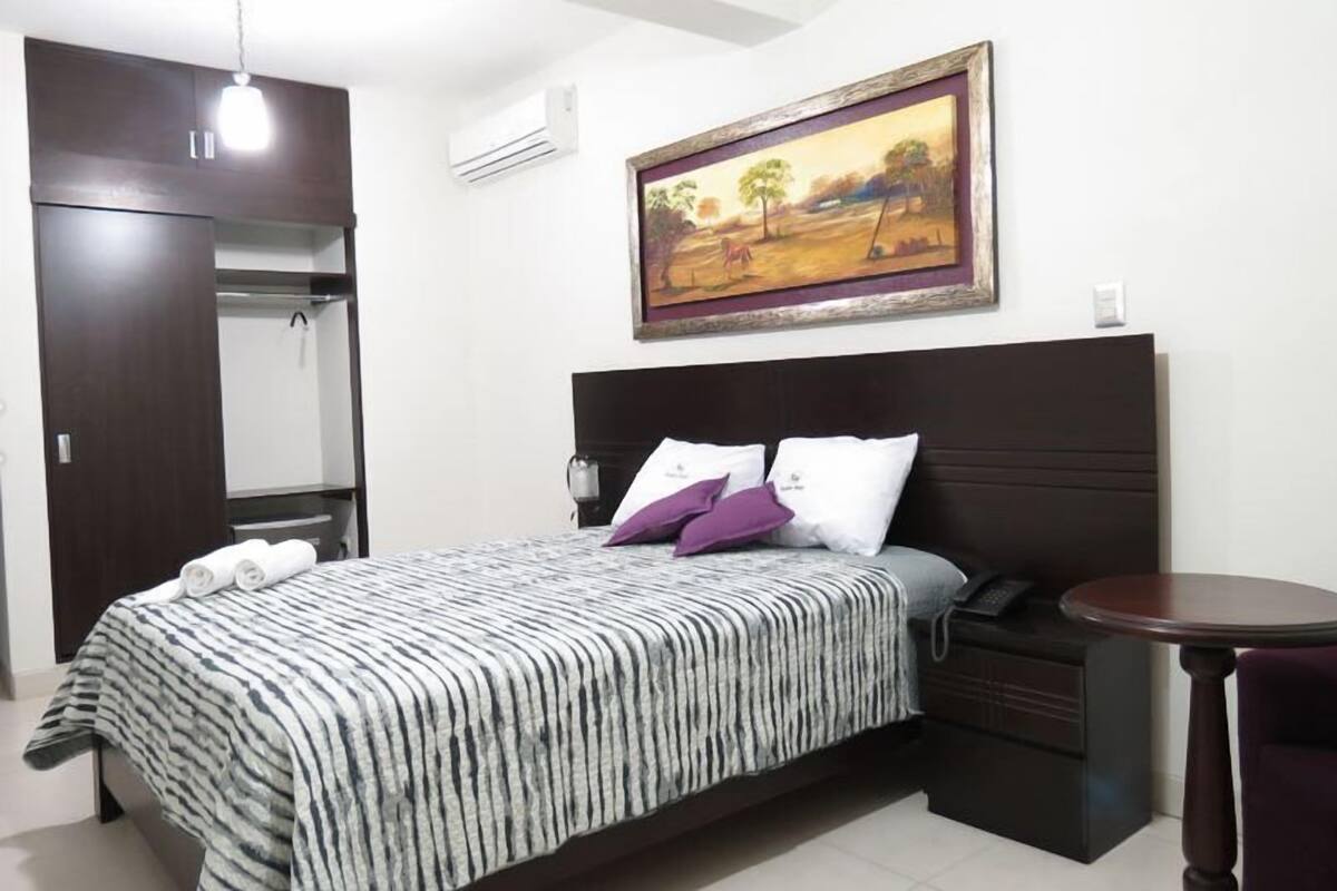 A bedroom with a bed, a bedside table, a chair, a painting on the wall, and a wardrobe.