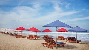 A beach with rows of wooden lounge chairs and umbrellas. - Hotel Amaris Kuta - Bali (Legian)