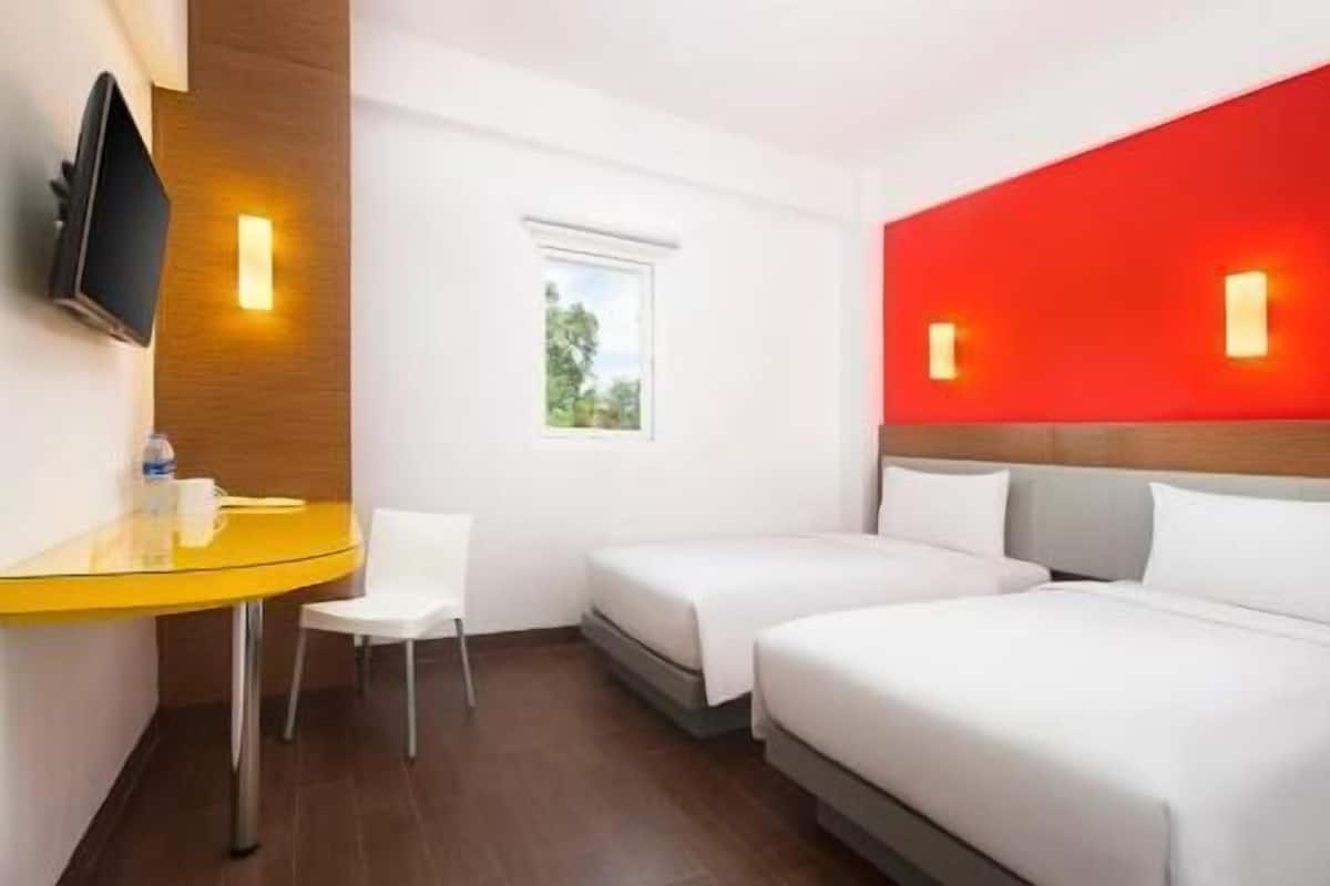 A hotel room with two beds, a desk, a chair, a TV, and a window.