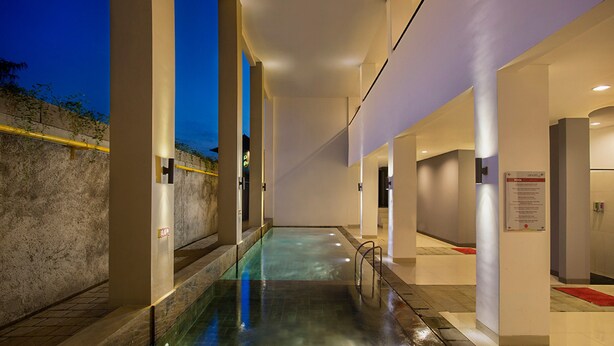 A modern indoor pool area with a glass barrier, a stone wall, and a red carpet. - Hotel Amaris Kuta - Bali (Legian)