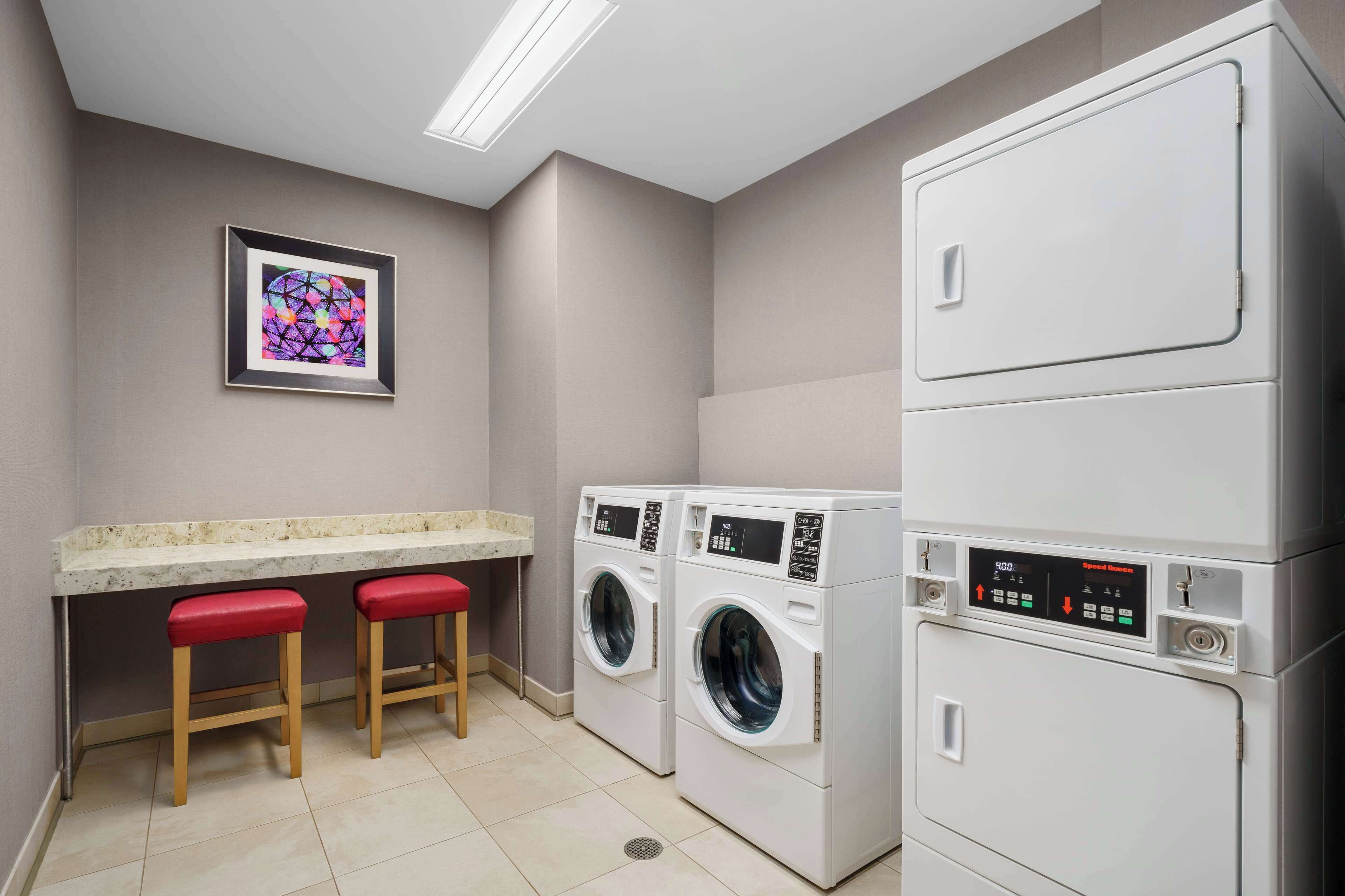A laundry room with two washing machines, a countertop, and two red stools.
