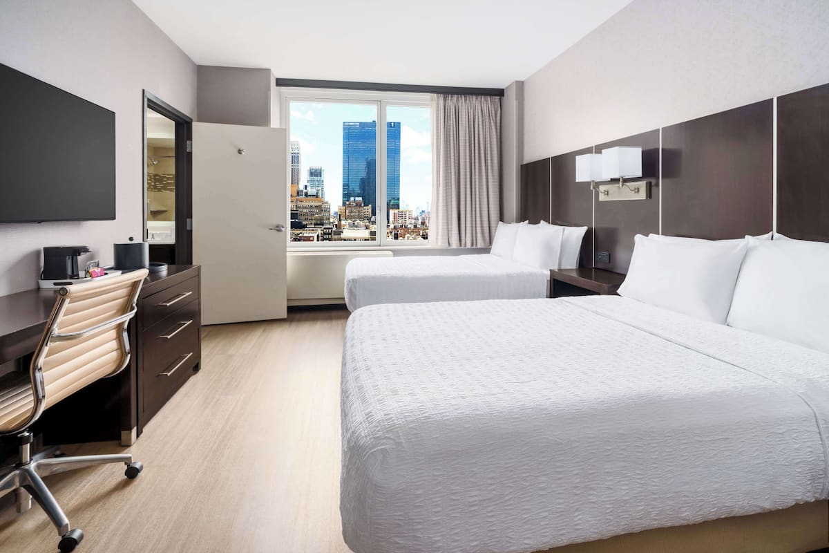 Une chambre d’hôtel avec un grand lit, un bureau avec une chaise, un téléviseur à écran plat et une vue sur la ville par la fenêtre.