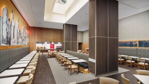 A modern restaurant with long tables and booths, a cityscape mural, and a skylight.