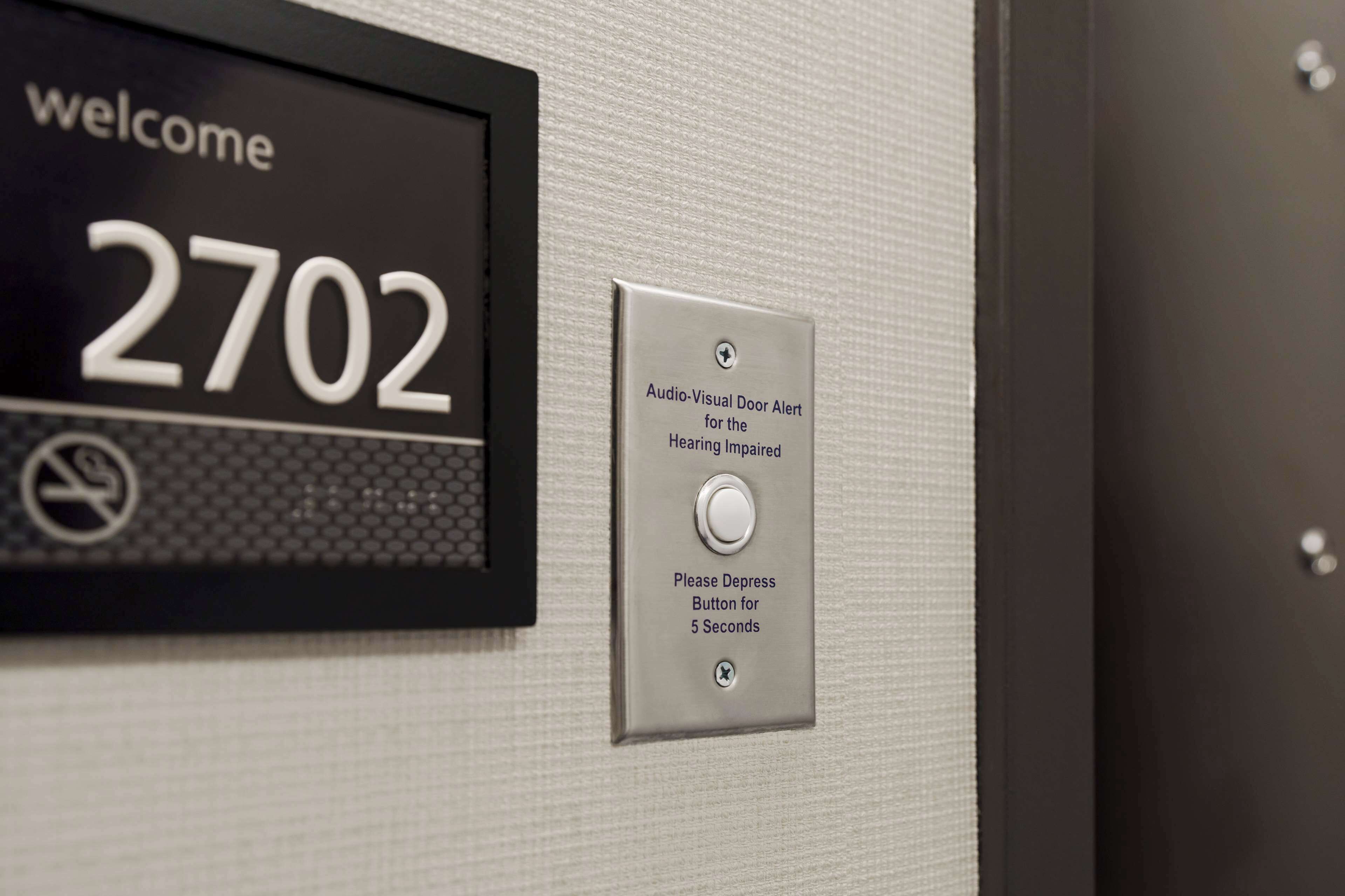 A welcome sign with the number 2702 and an audio-visual door alert sign for the hearing impaired.