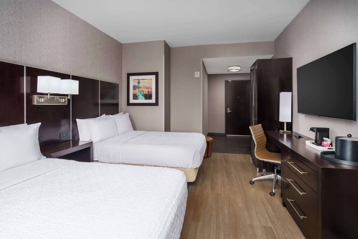 Une chambre d’hôtel avec deux lits, un bureau avec une chaise, une télévision et un tableau encadré au mur.