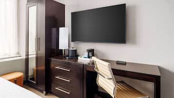 Habitación de hotel con cama, escritorio con silla, armario, televisor de pantalla plana y cafetera.