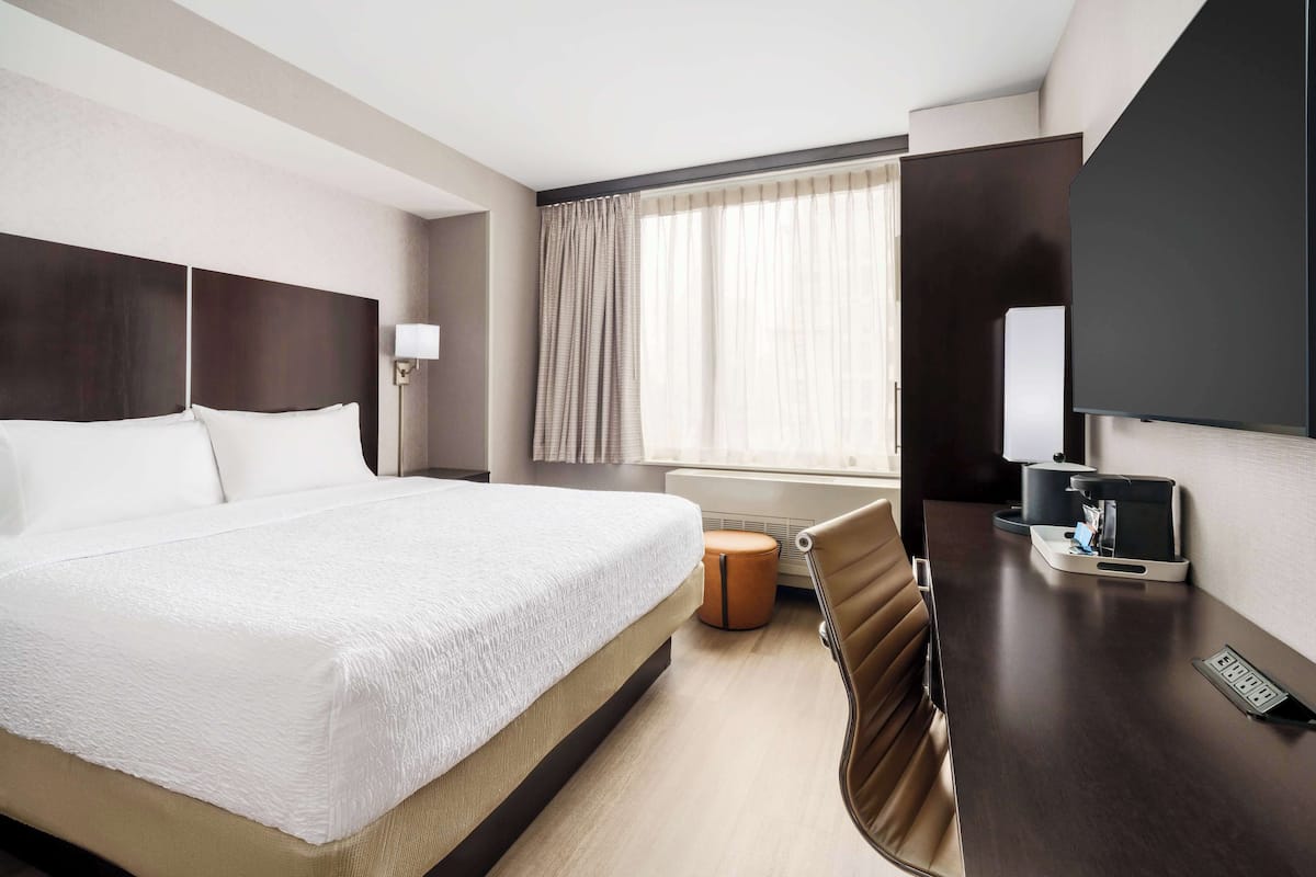 Une chambre d’hôtel avec un grand lit, un bureau avec une chaise, une télévision et une fenêtre avec des rideaux.