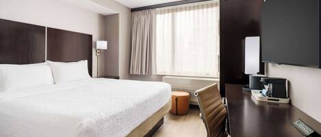 Una habitación de hotel con una cama grande, un escritorio con silla, un televisor y una ventana con cortinas.
