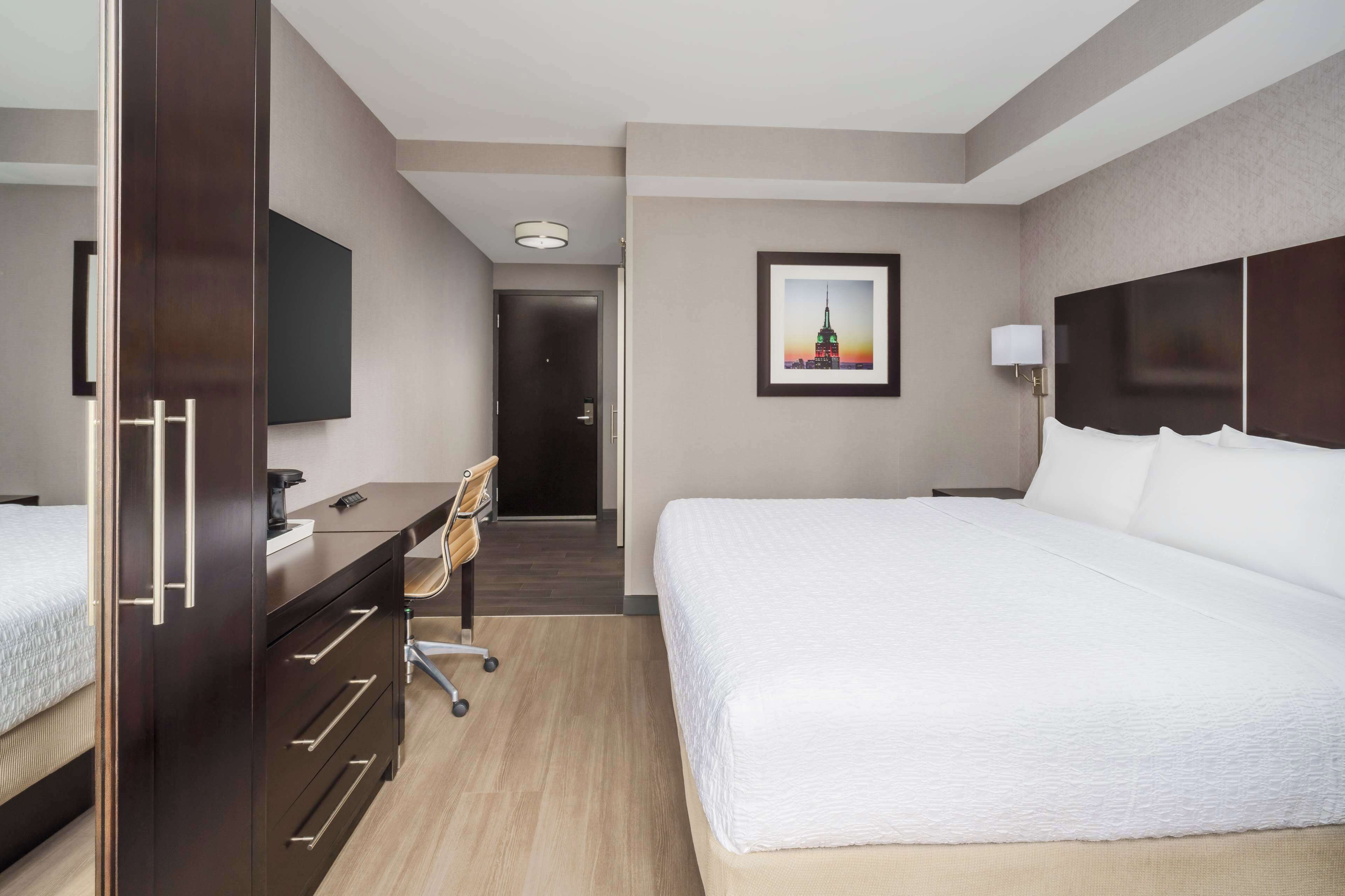 A hotel room with a large bed, a desk with a chair, a television, and a framed picture on the wall.