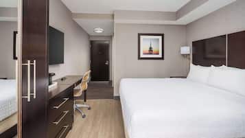 A hotel room with a large bed, a desk with a chair, a television, and a framed picture on the wall.